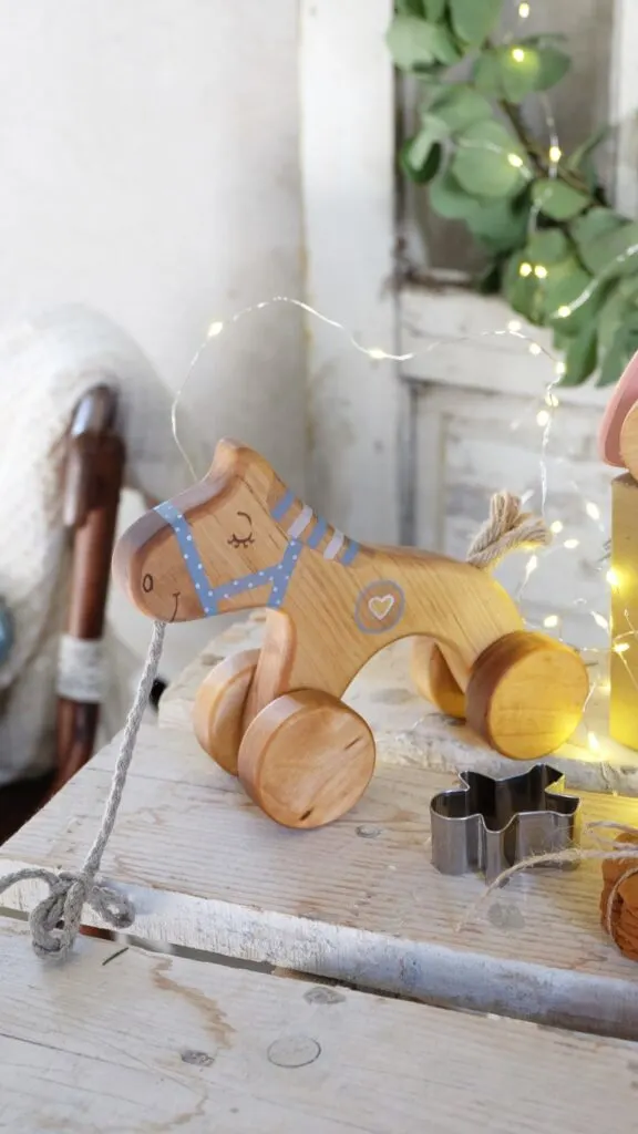 Wooden horse pull toy sitting on an end table with twinkle lights in the background