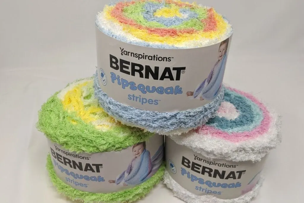 bernat pipsqueak stripes yarn cakes in three different colorways stacked together against a white background