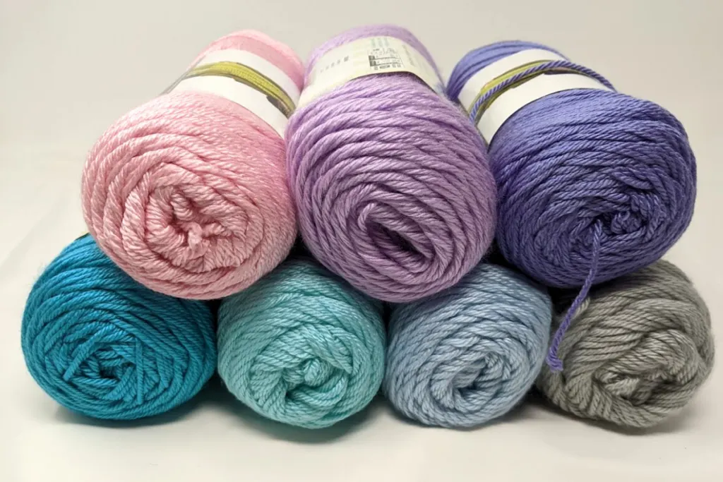 caron simply soft yarns stacked on top of each other in colors from left to right, top to bottom, soft pink, orchid, lavender blue, ocean, mint, soft blue, feathered gray