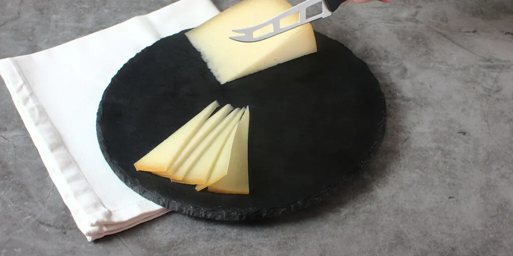 A woman cutting pieces of idiazabal cheese on stone