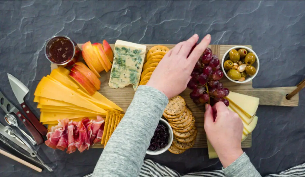 Arranging gourmet cheese, crackers, and fruits on a board for a large cheese board.