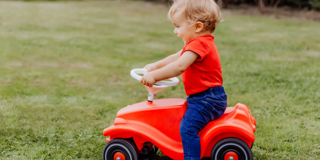 Baby girl riding toy car in garden