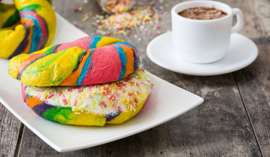 Colorful bagels with cheese and sprinkles and coffee on a wooden table