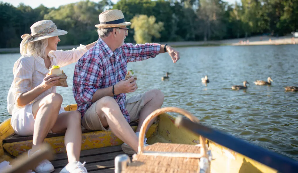 Couple sitting on the boad feeding ducks with their bread