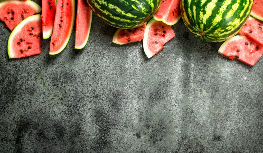 Fresh ripe watermelon slices and whole watermelon on gray background