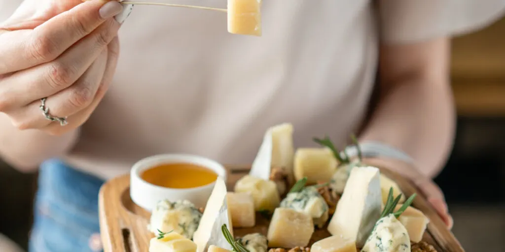 Girl holding piece of parmesan cheese on a skewer and wooden plate with cheese