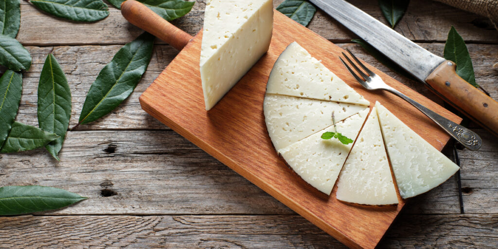 Slices of cured Manchego cheese on a wooden board with a rustic background