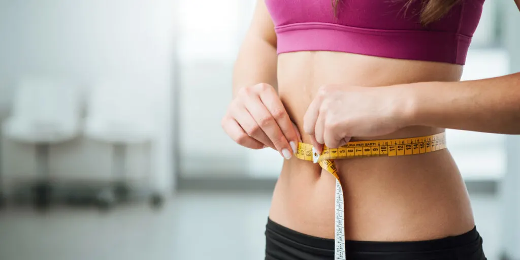 Slim young woman measuring her thin waist with a tape measure