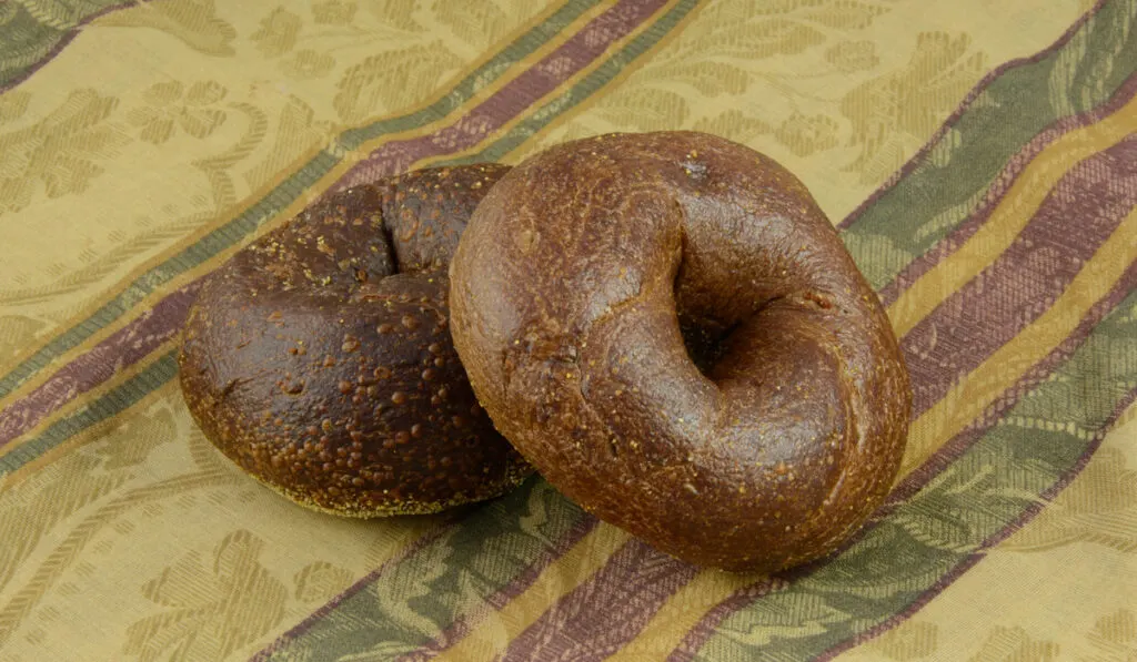 Two whole pumpernickel bagels on tablecloth