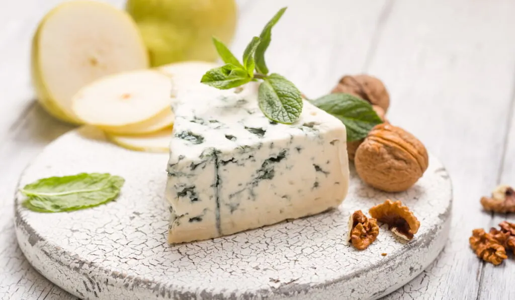 blue goat cheese with some mint leaves and walnuts on a white wooden board