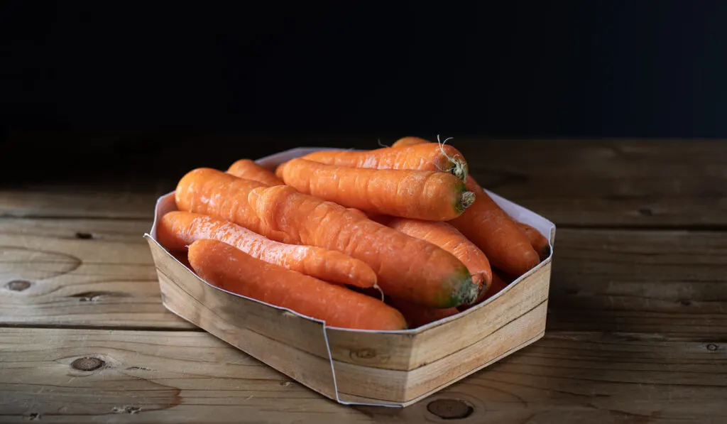 bunch of carrots in a paper basket on wooden table 