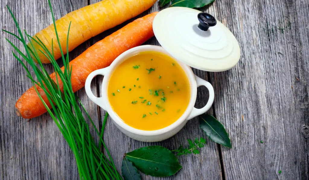 carrot soup in a bowl and fresh raw carrots and leaves