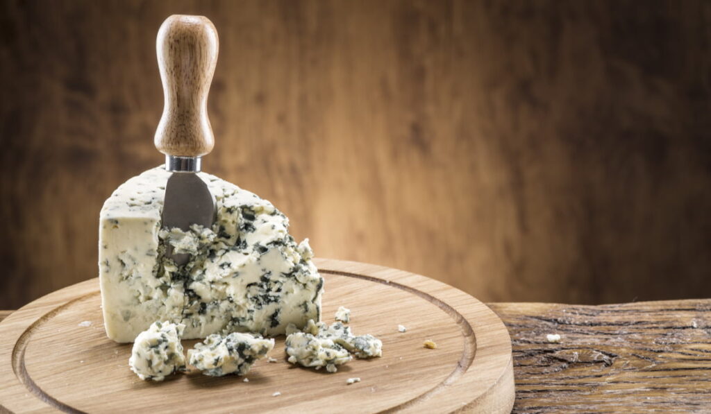 cheese knife stuck in a sliced blue cheese on a wooden board 