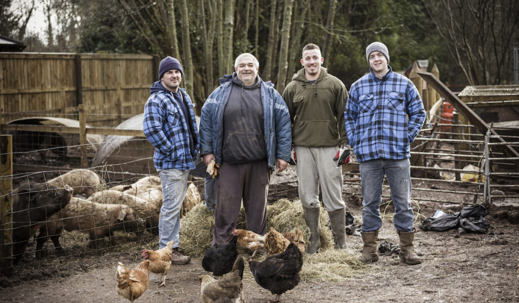 four men standing with chicken and pigs on background