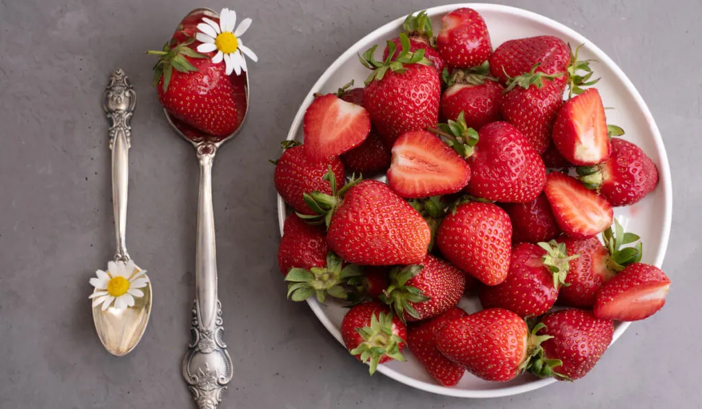 fresh strawberries on white plate with spoons and flowers