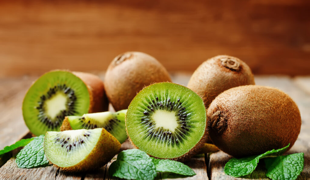 fresh whole and sliced kiwi with leaves on wooden table