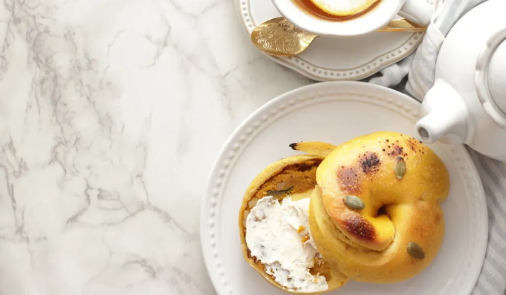 pumpkin bagel with cream cheese on a white plate and a tea