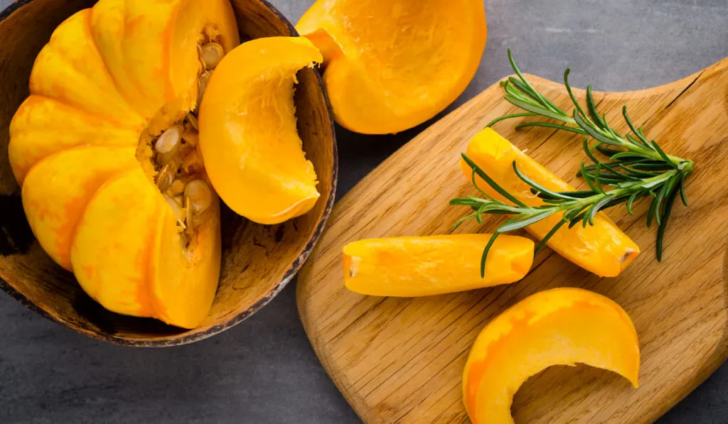 sliced pumpkin with rosemary on wooden bowl and chopping board