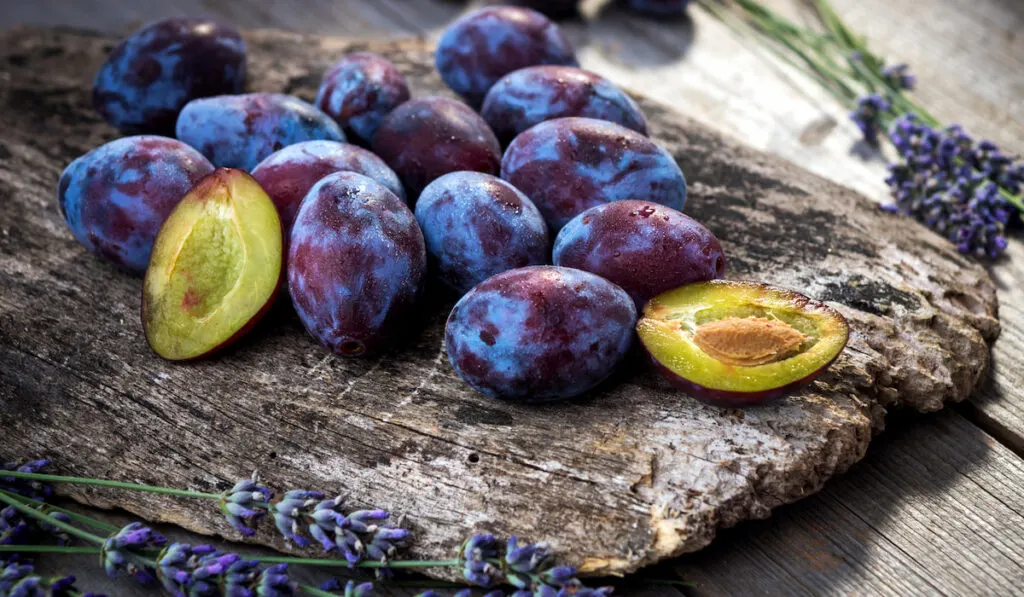 whole and sliced fresh plums on wooden board