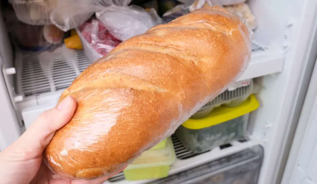 woman's hand putting a loaf of wheat bread in the fridge