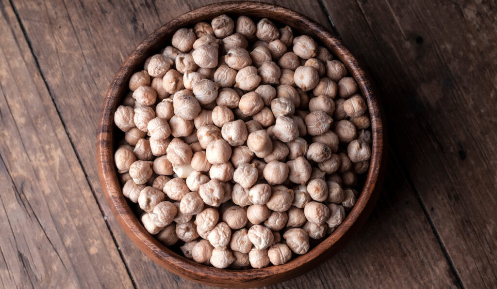 A wooden bowl of raw chickpeas on wooden background 