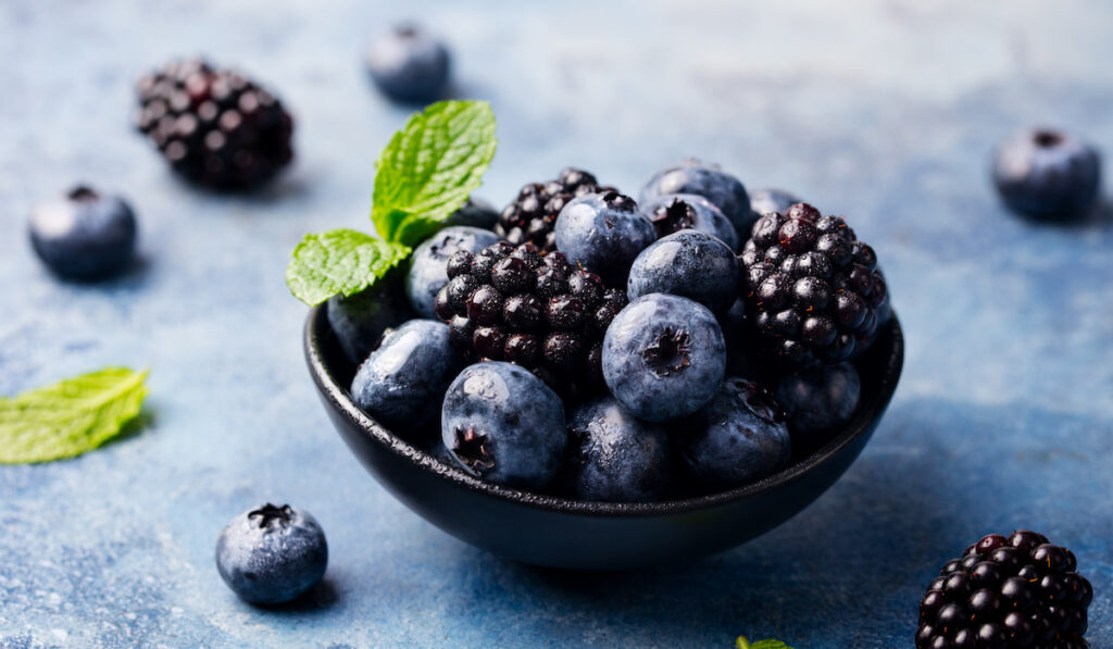 Blueberry and blackberry berries in black bowl on blue stone background 