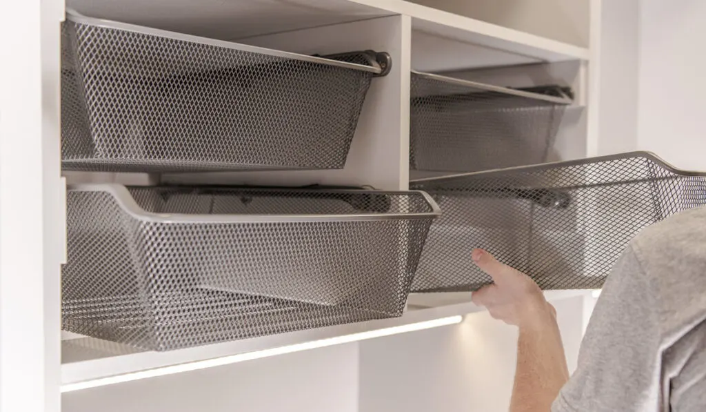 Closeup of man instaling storage wire basket in adjustable shelf