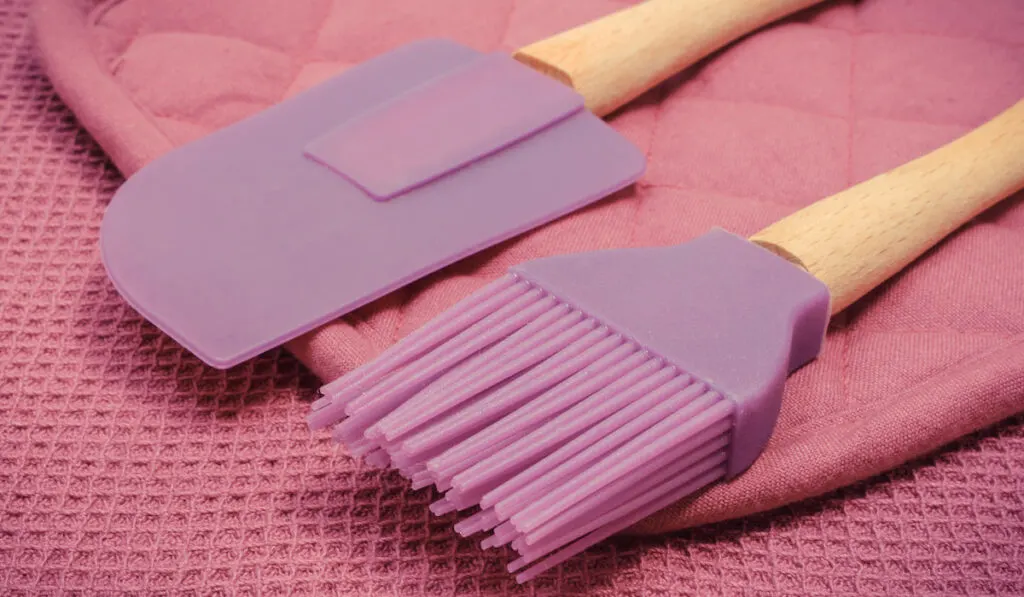 Closeup of silicone half spatula and brush on pink background 
