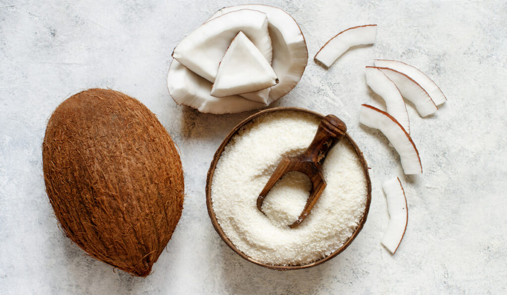 Coconut flour in a wooden bowl with coconut pieces on white background 