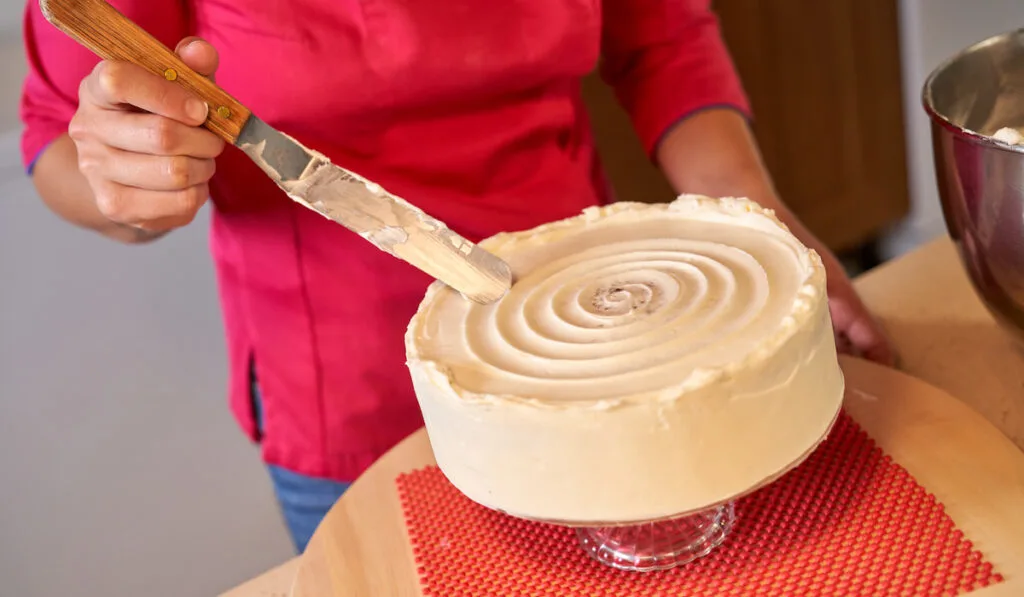 Crop female confectioner decorating cake using offset spatula 