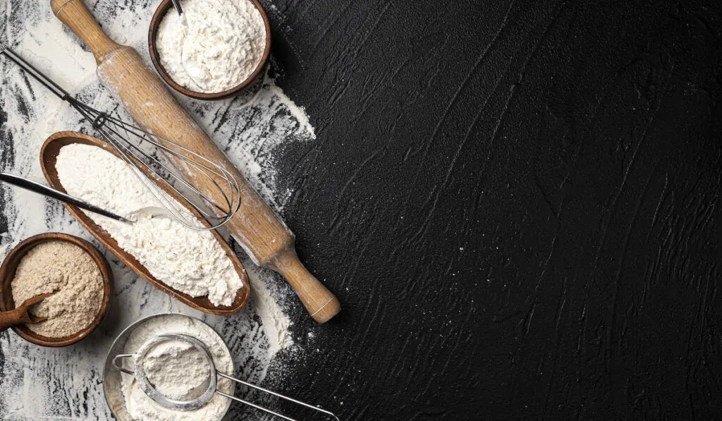 Different types of flour in wooden bowls on black table 