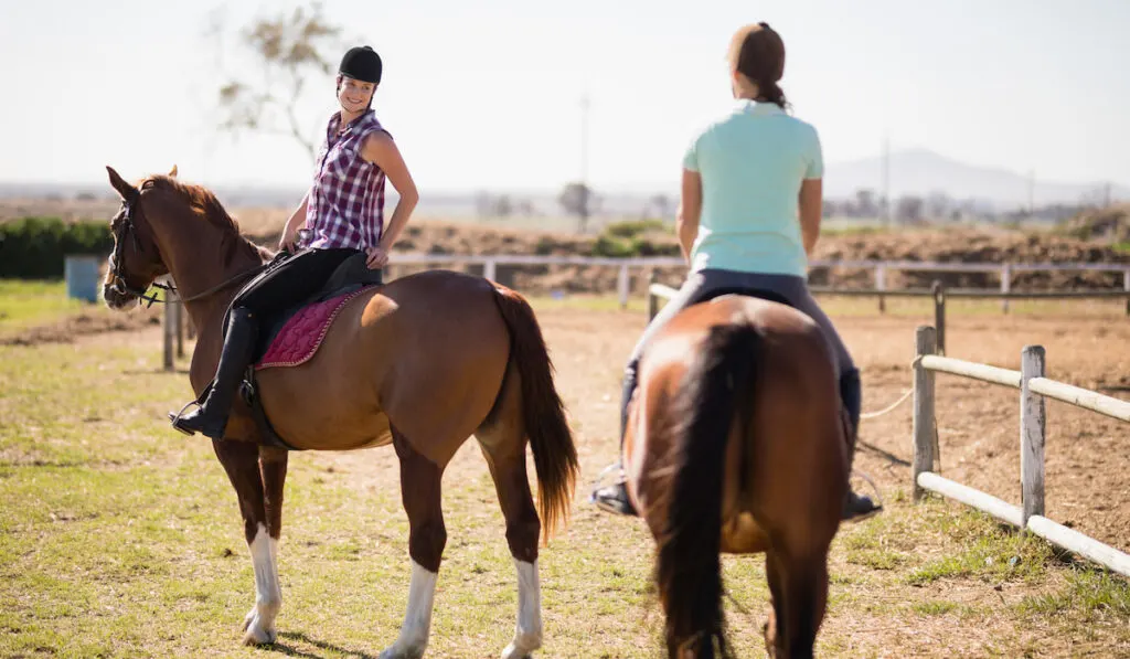 Female friends horseback riding on field 
