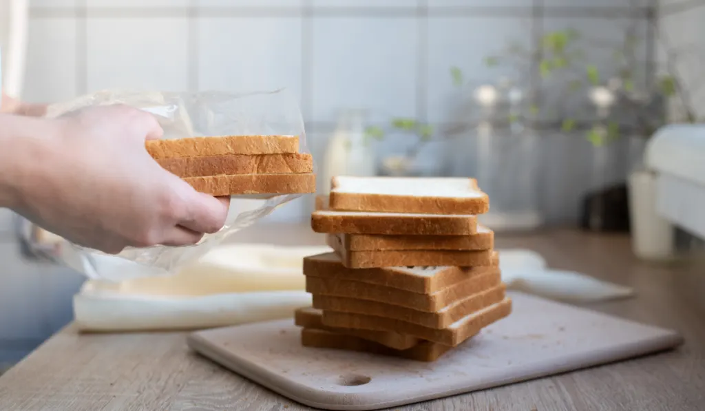 Female hands taking out slices of bread from a package on the kitchen table