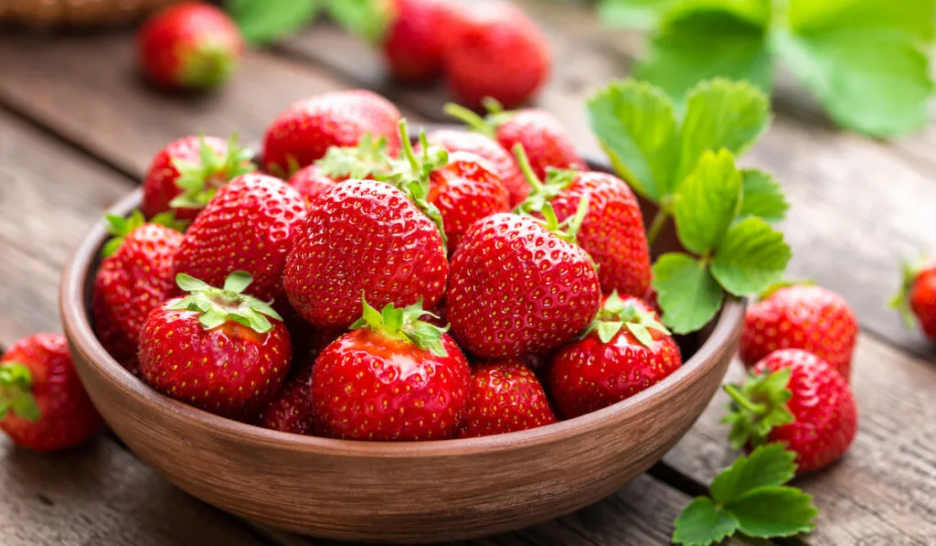 Fresh juicy strawberries with leaves in wooden bowl
