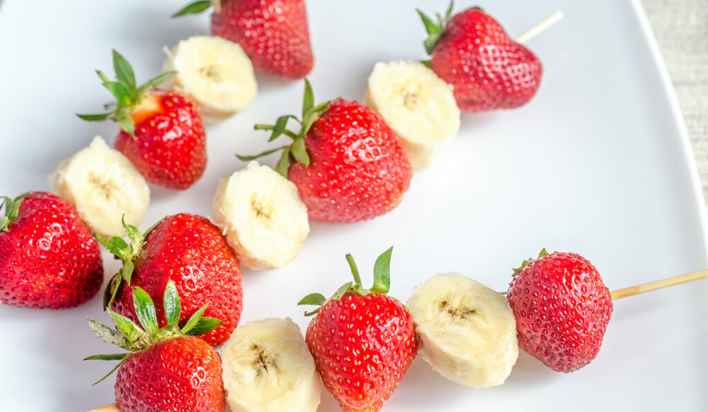 Fresh strawberry and banana skewers on white plate 