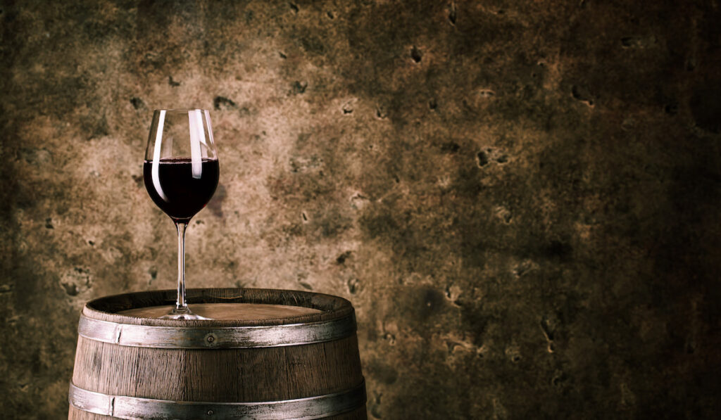 Glass of red wine on wine barrel on rustic background