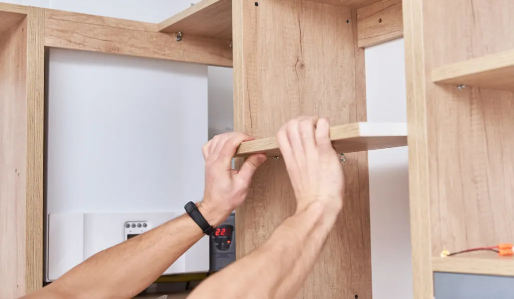 Male carpenter install shelf in kitchen cabinet