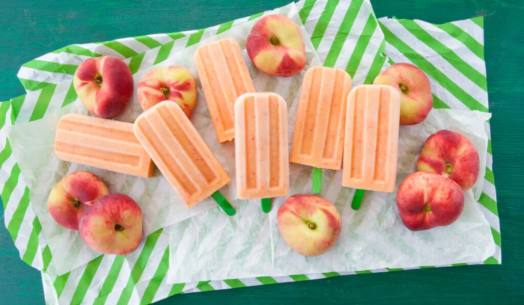 Peach popsicles and whole peaches on green table 