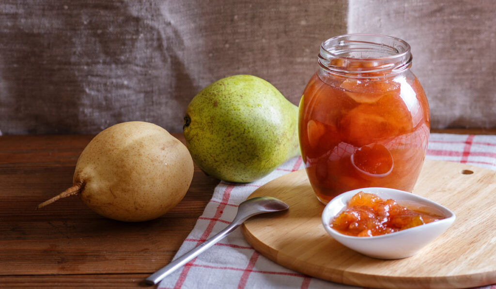 Pear jam in a glass jar on a linen tablecloth on a wooden table.