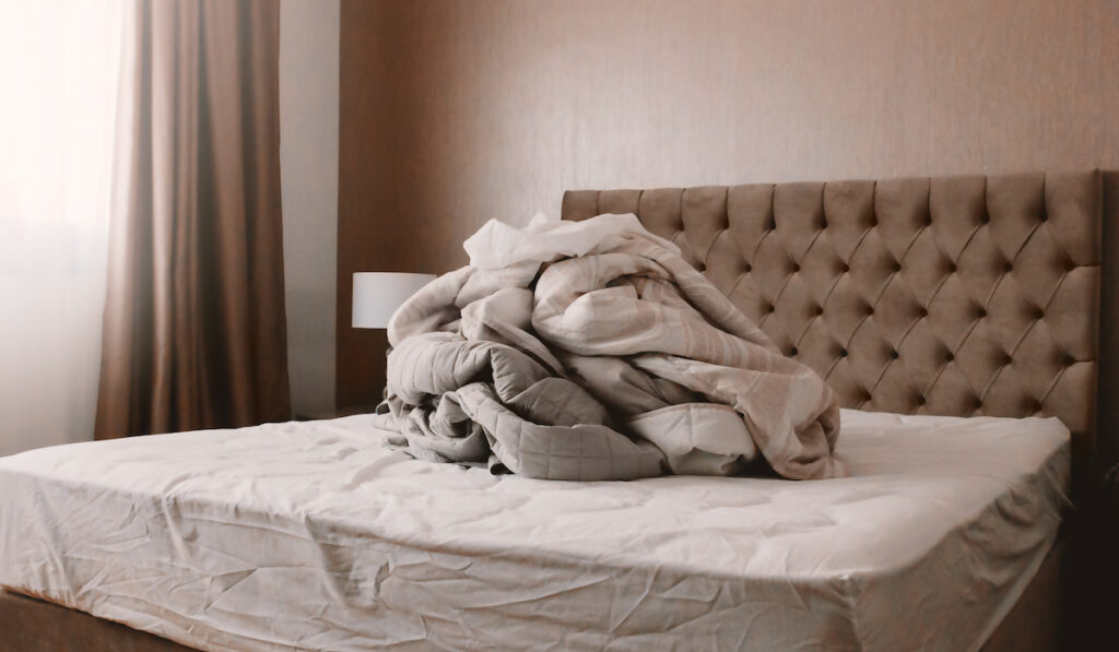 Pile of dirty linen on bed in bedroom with modern interior in neutral colors 