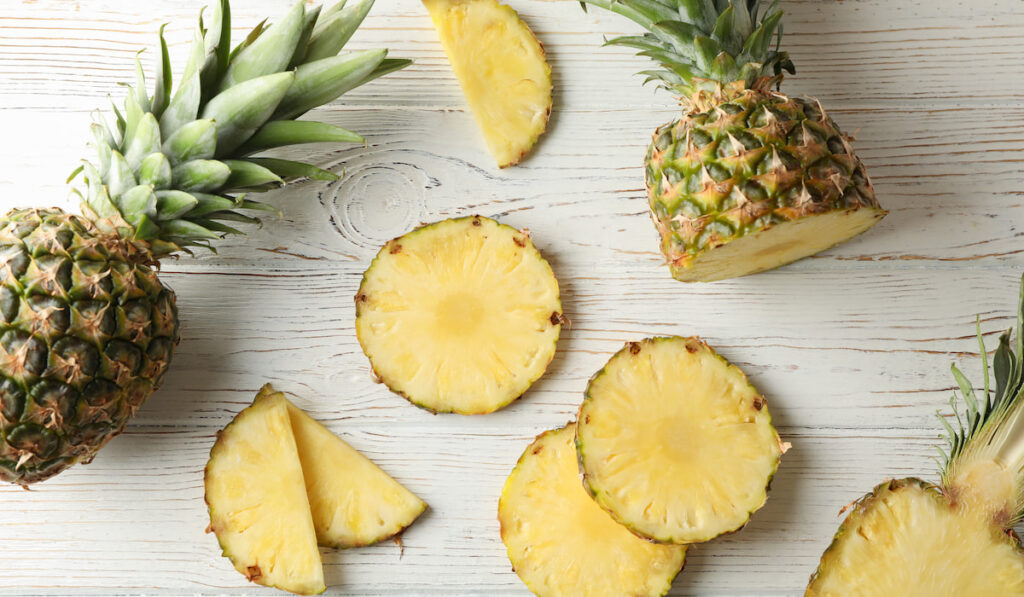 Pineapples and slices on white wooden background