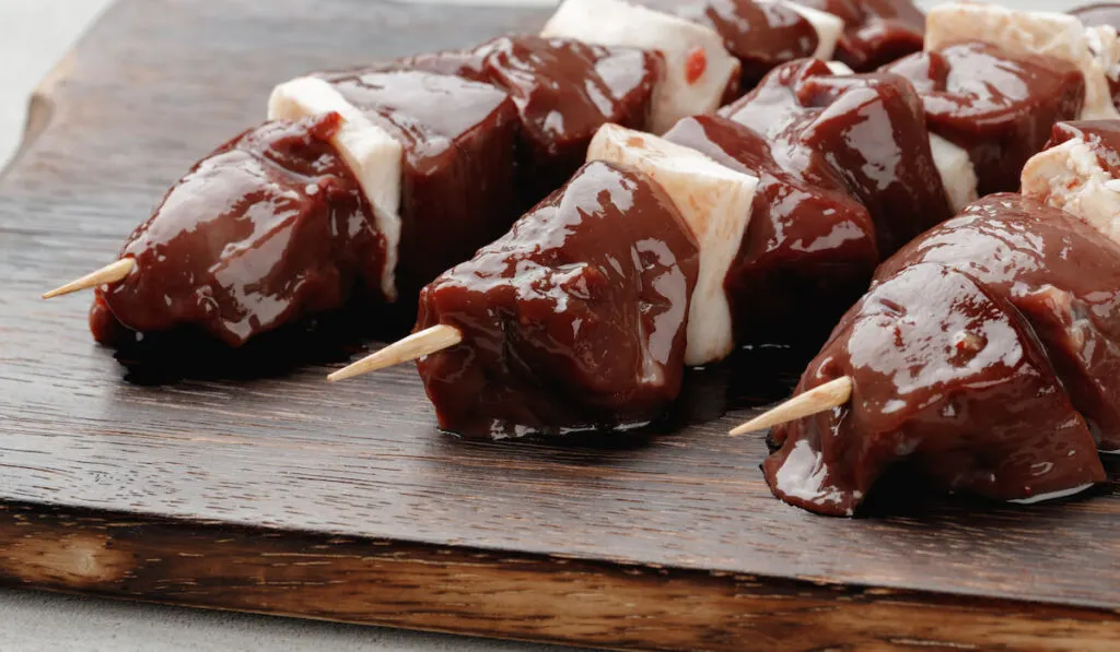 Raw beef liver on skewers on wooden choppingboard 