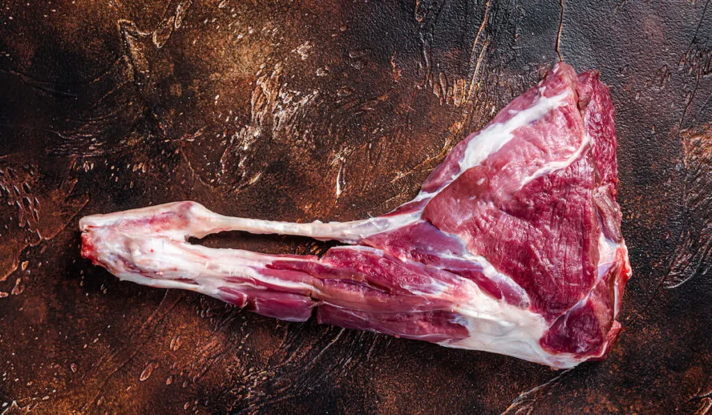 Raw goat leg meat on the bone. Dark background 