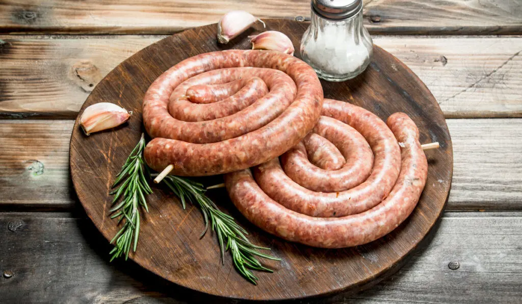 Raw sausage with rosemary and garlic on wooden table 