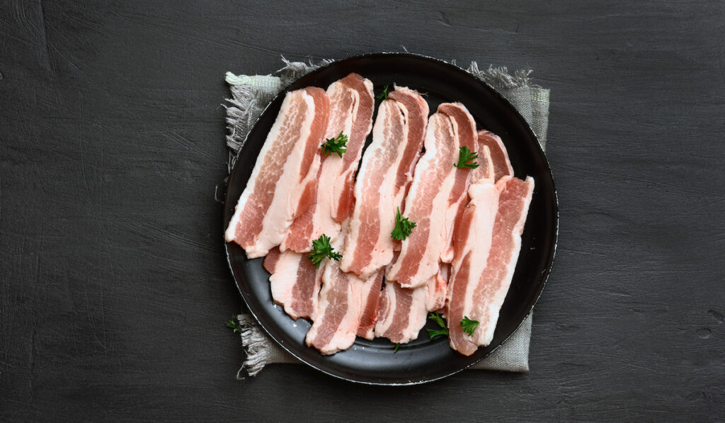 Raw sliced bacon in black plate on black background