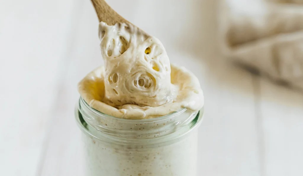 wooden spoon mixing a sourdough starter in a glass jar