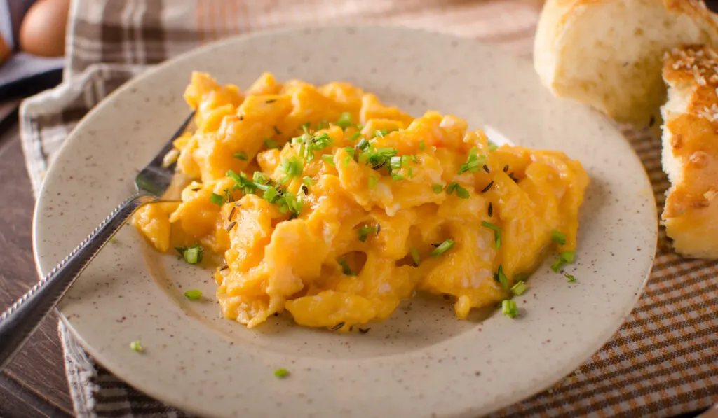 Scrambled eggs on plate with fork and buns on side 