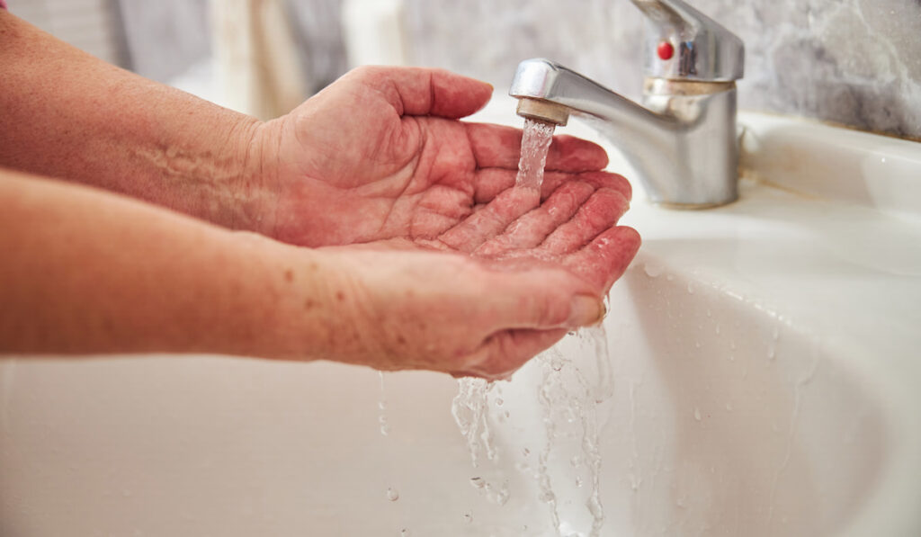 Senior woman washing hands under running water from the faucet sink 