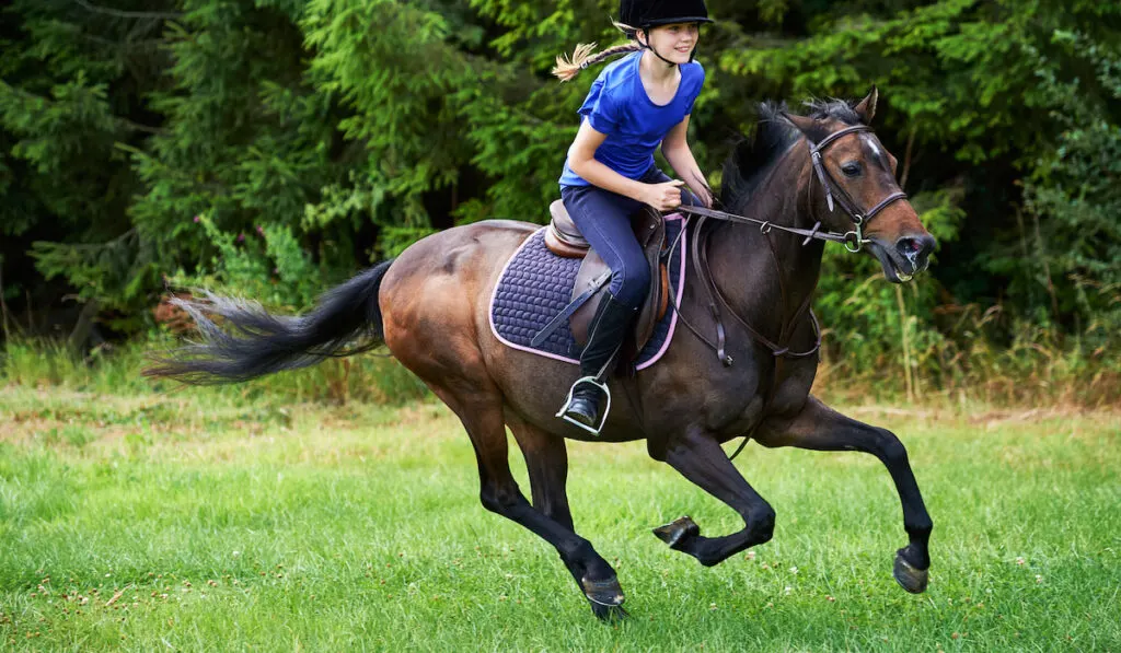 Side view of girl wearing riding hat galloping on horseback 
