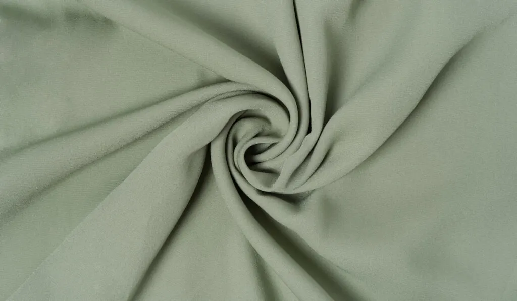 Soft green deluxe quality polyester fabric is rolled up in beautiful waves